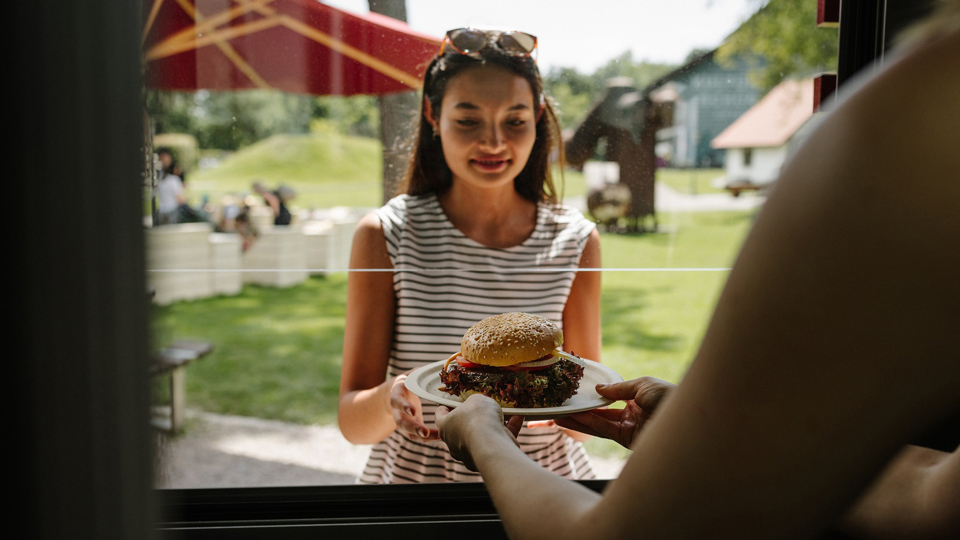 Eine Frau nimmt einen Burger bei der Essensausgabe vom Bahnhöfli entgegen.