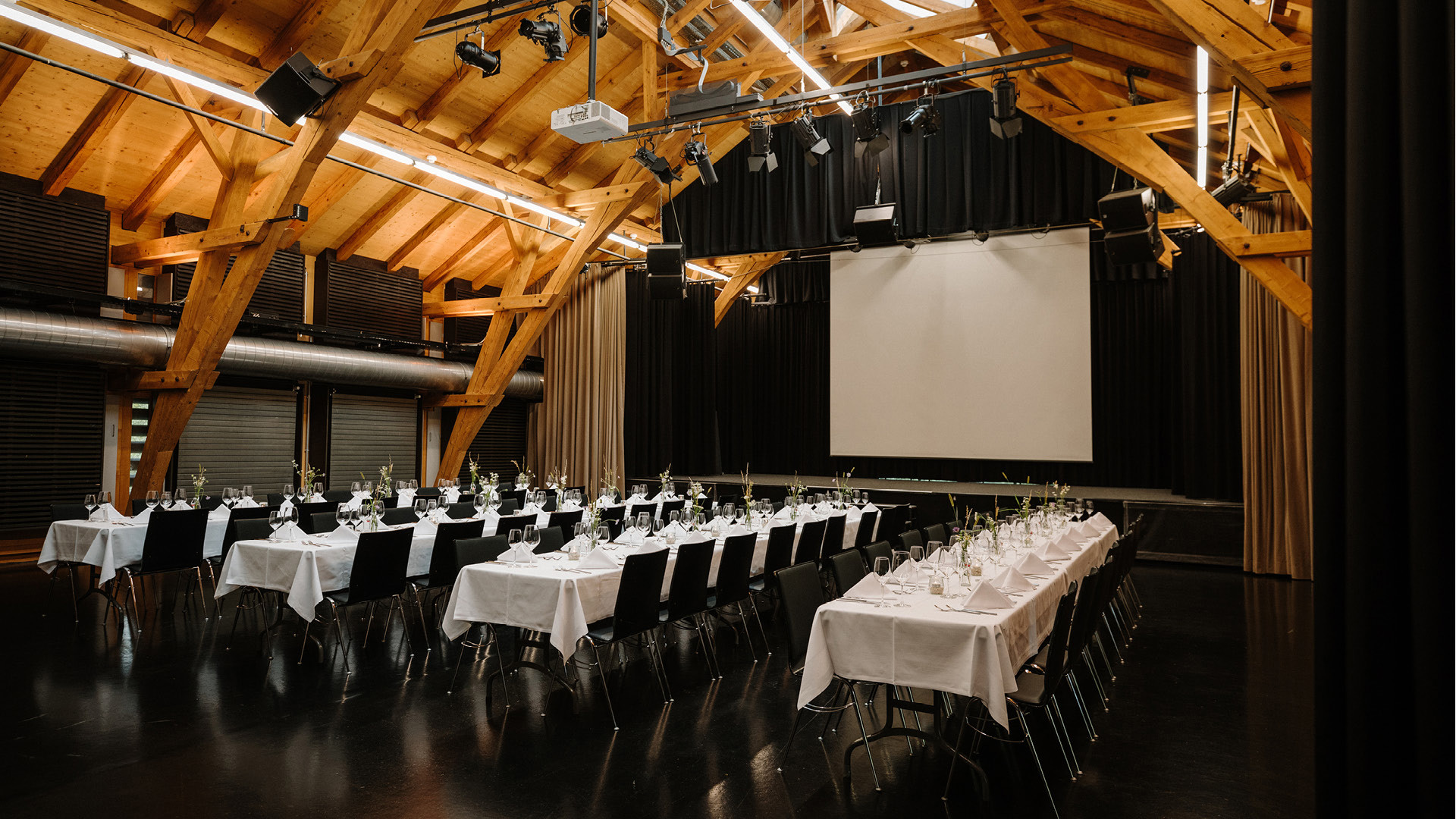 Das Obergeschoss von der Eventlokalität Schüür mit vier langen Tischreihen, die für ein Nachtessen gedeckt sind.