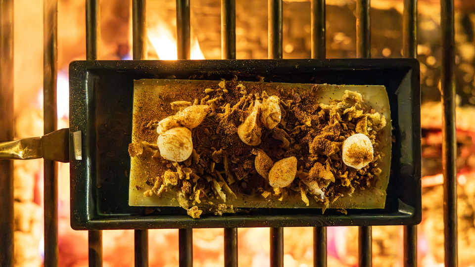 Raclette-Käse mit Beilagen über offenem Feuer im Winterdorf auf dem Gurten.