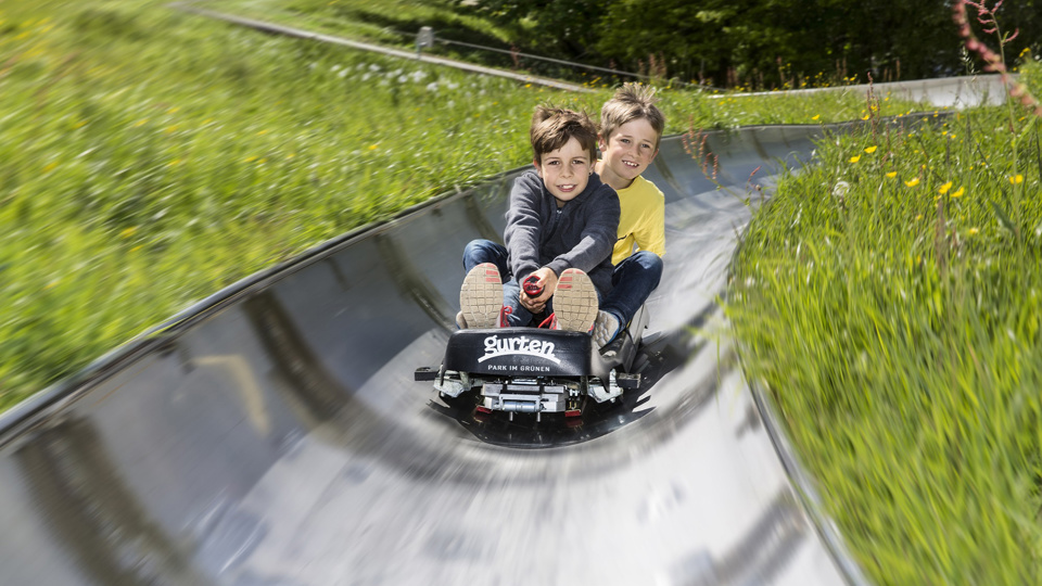 Zwei Kinder sausen auf dem Schlitten die Rodelbahn hinunter