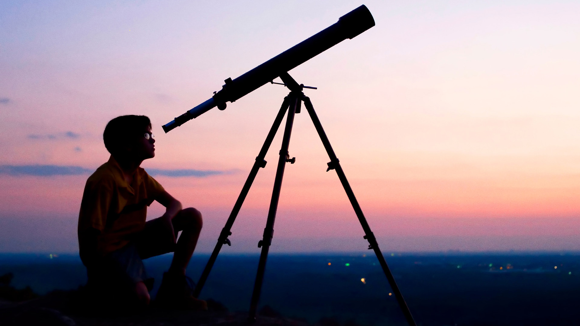 Ein Kind welches vor einem roten Himmel durch ein langes Teleskop den Himmel betrachtet.