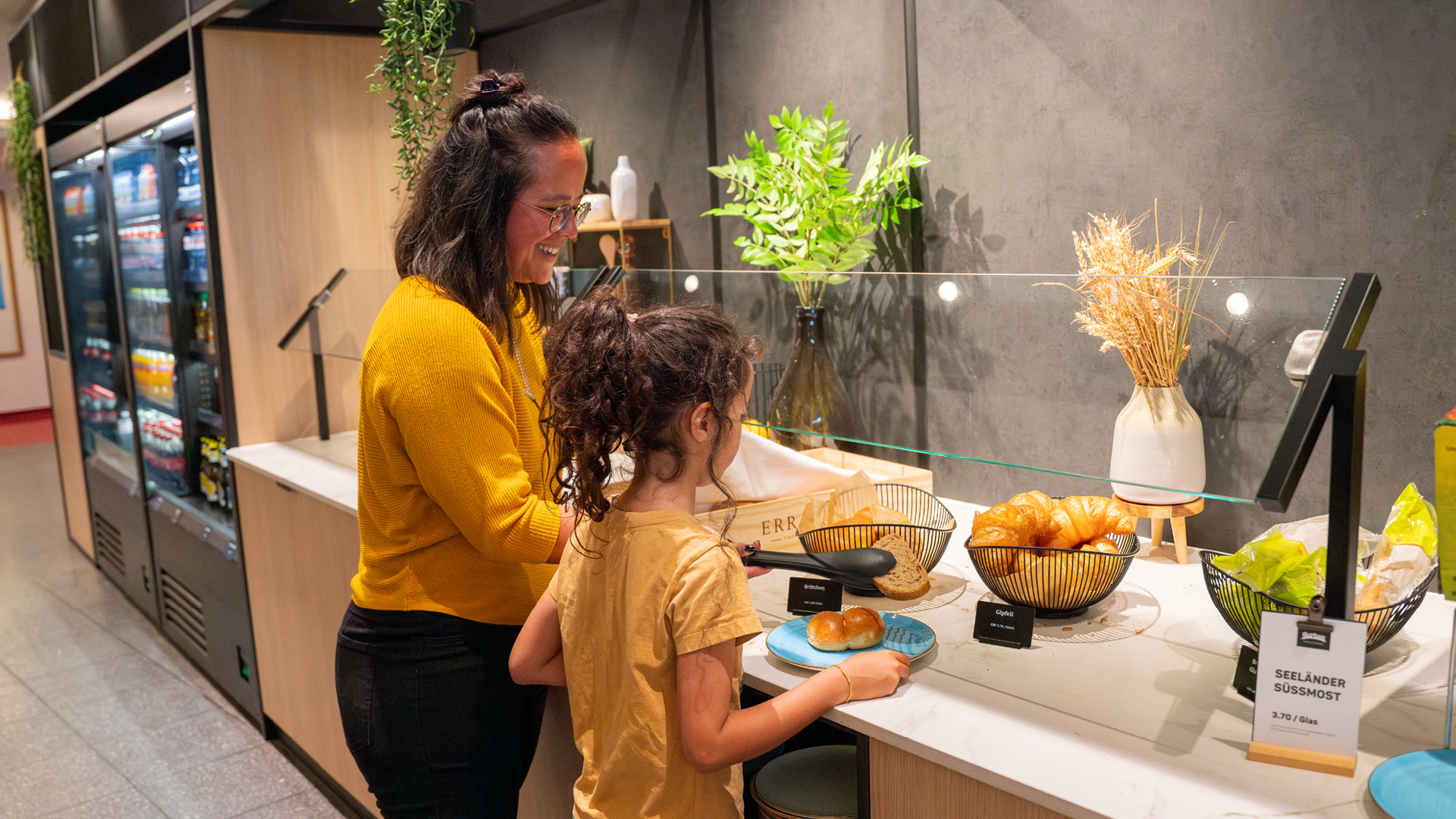 Zwei Personen welche sich beim Brunch im Huusbüffe Brot auf das Teller legen. Sie tragen beide ein gelbes Oberteil.