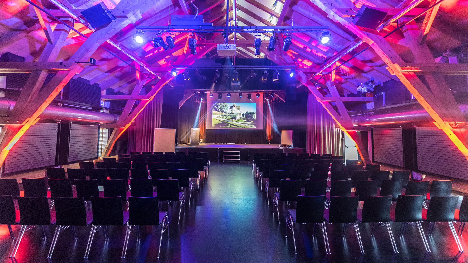 Farbig ausgeleuchtete Schüür mit Konzertbestuhlung