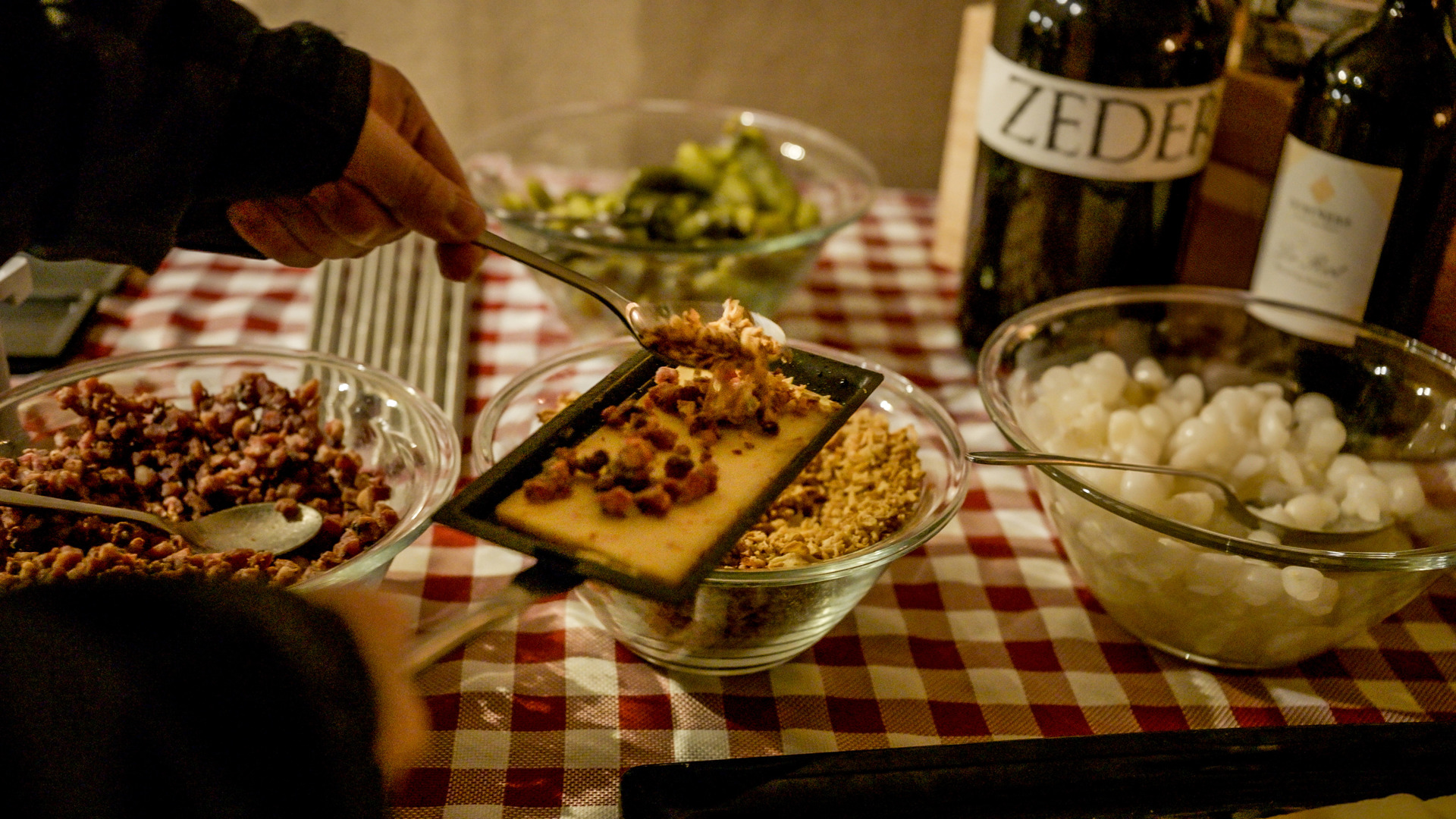 Jemand gibt Zutaten auf eine Racletteschale