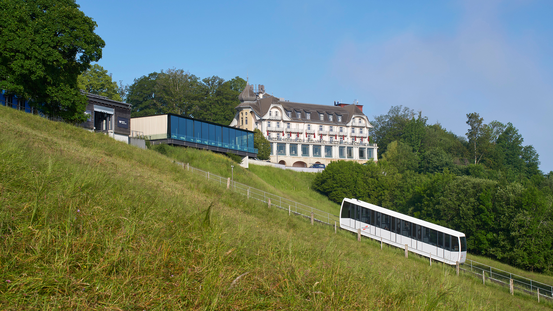 Die Gurtenbahn bei Tag vor dem Kulm-Gebäude und der Eventlocation Pavillon.