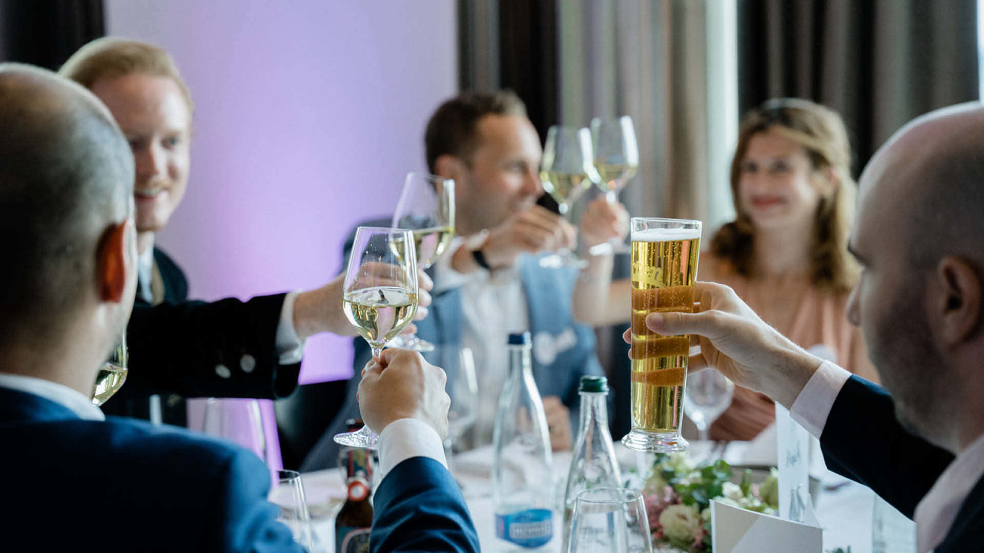 Eine Gruppe stosst mit Wein- und Biergläser an einem Tisch an.