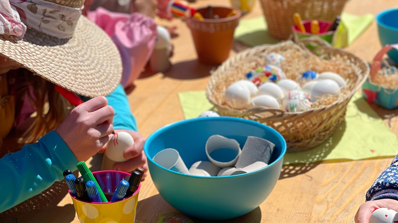 Mehrere Kinder welche Eier bemalen auf einem Tisch mit anderen Zeichenutensilien.