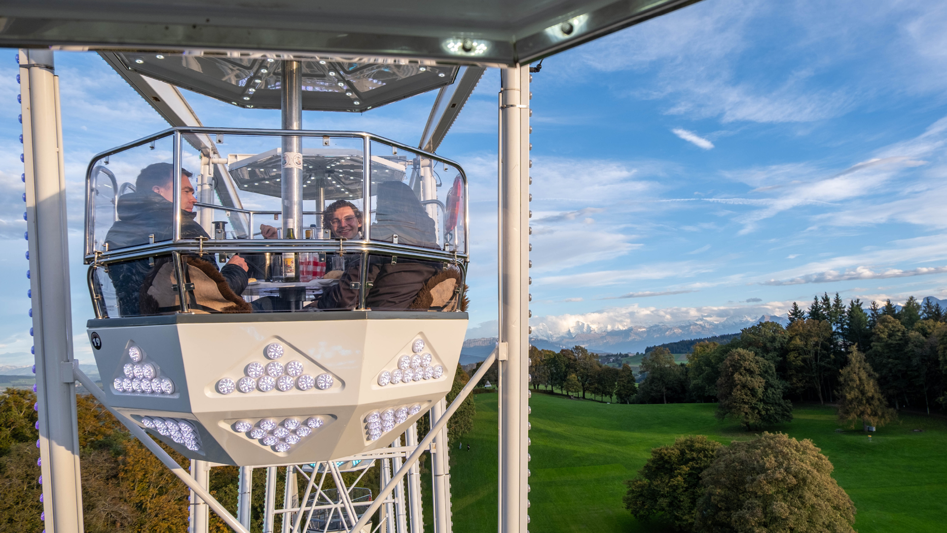 Drei Personen sitzen im Riesenrad und geniessen die Aussicht.