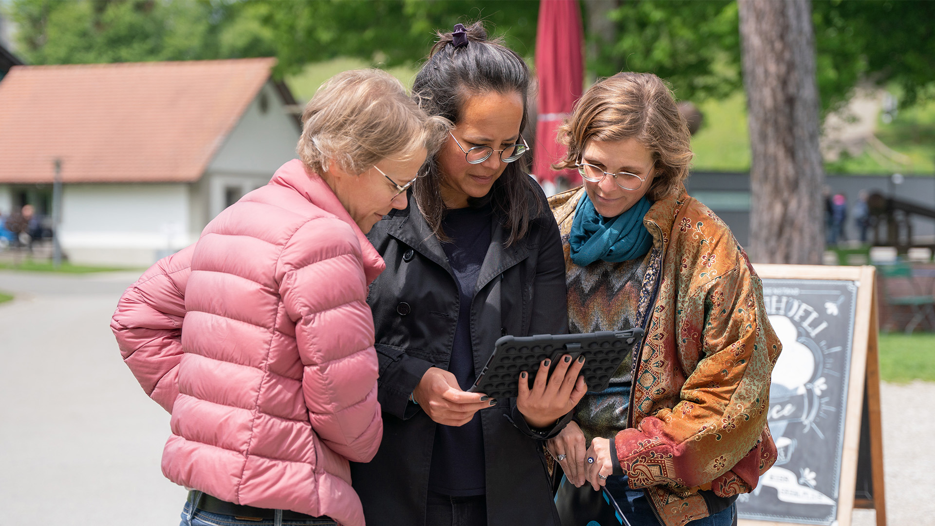 Drei Frauen schauen auf ein Tablet im Garten des Gurten.
