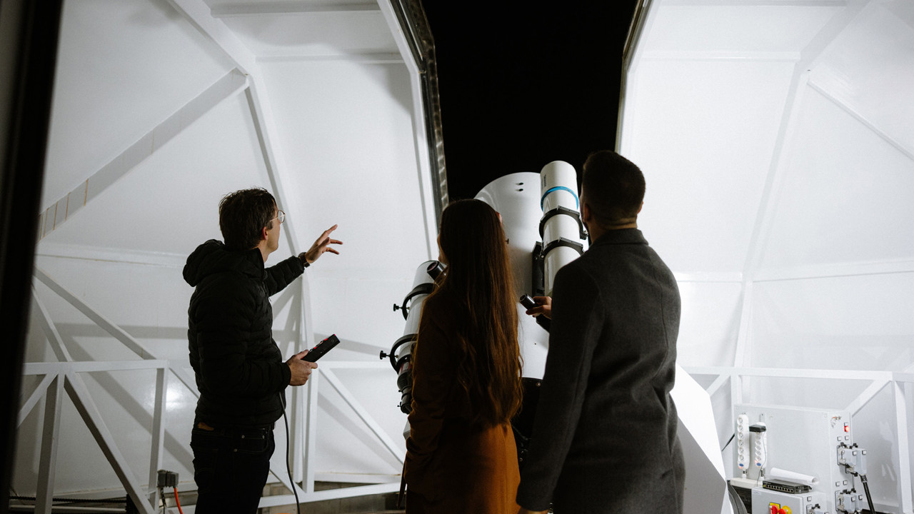 Das Innenleben der Sternwart mit dem grossen Teleskop. Ein Experte von Astro Event erklärt zwei Personen den Nachthimmel.