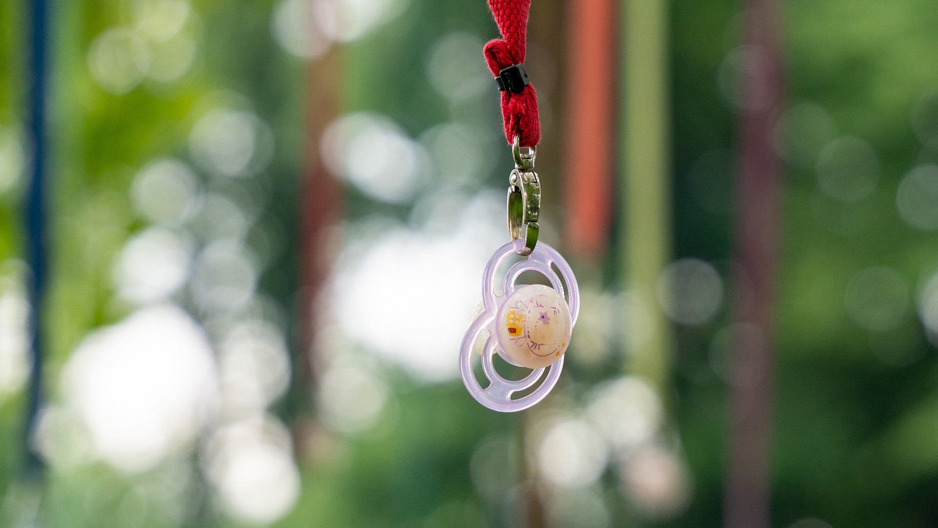 Violetter Schnuller am Nuggibaum mit rotem Bändel