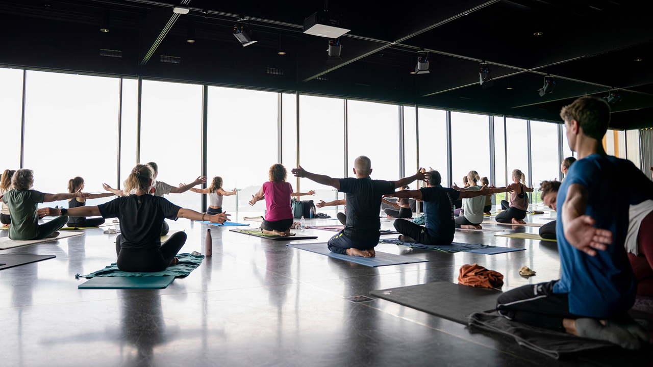 Mehrere Personen welche beim Yogabrunch auf Yogamatten sitzen und die Arme von Körper wegstrecken.