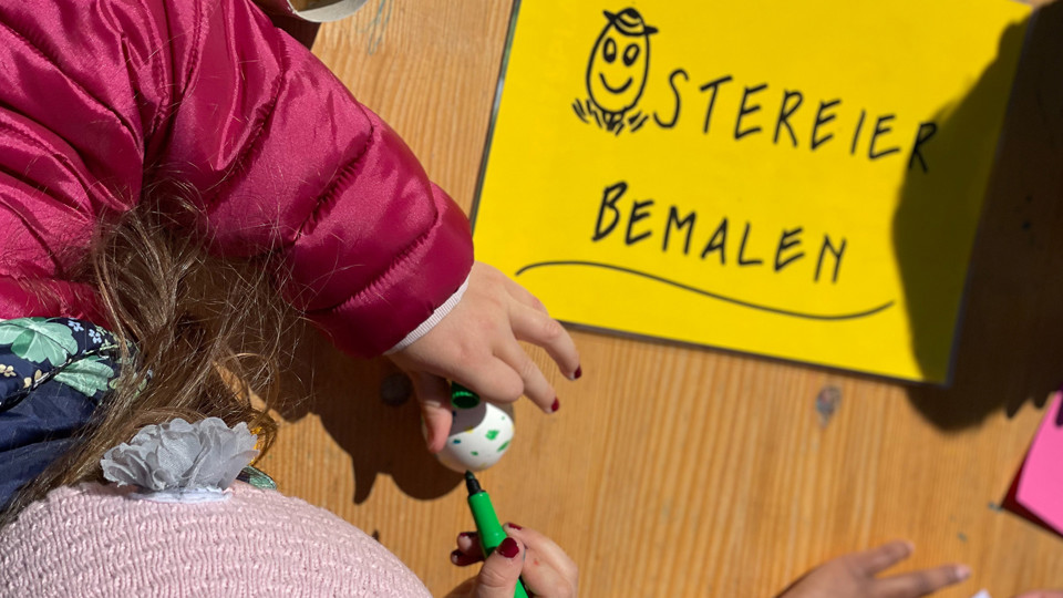 Ein Kind welches ein Ei mit einem grünen Stift bemalt.