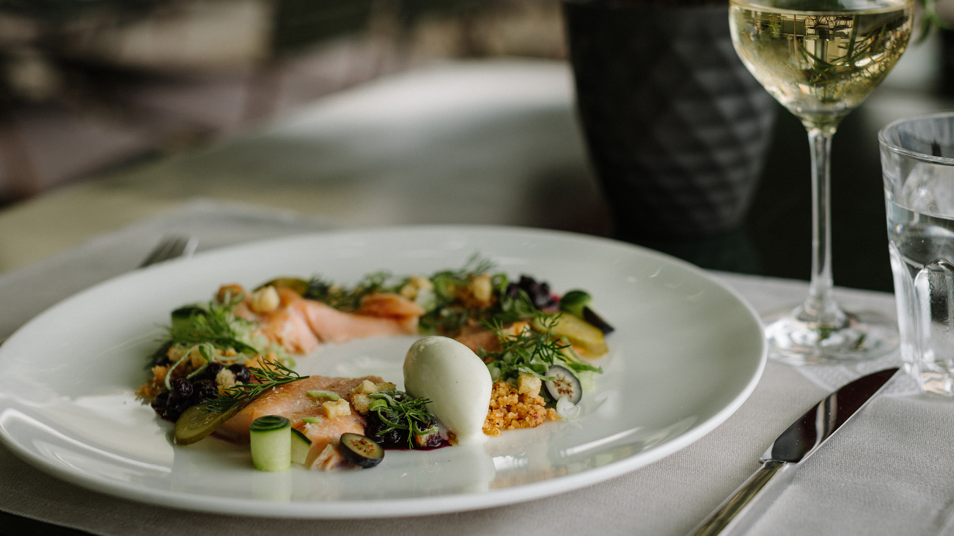 Kaltes Fischgericht auf weissem Porzellanteller mit einem Glas Weisswein