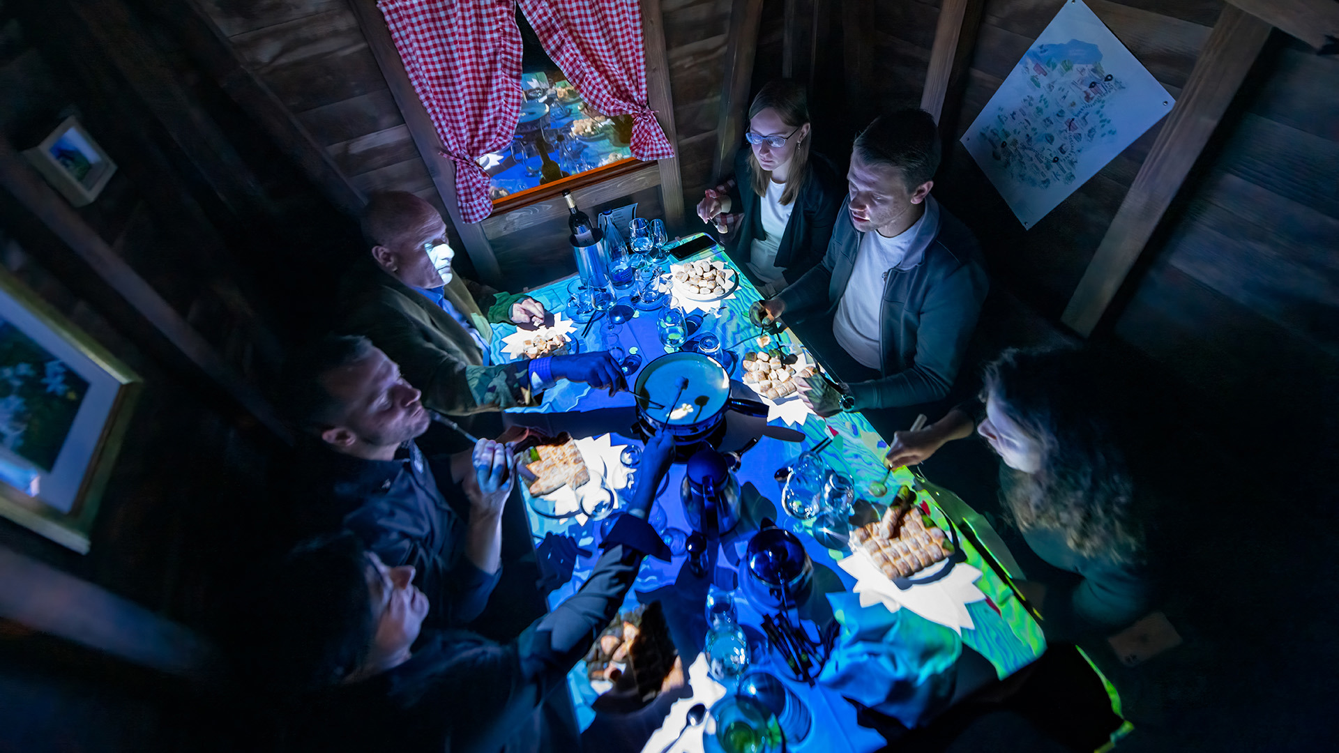 Sechs Personen essen in einem kleinen Holzchalet ein Fondue.