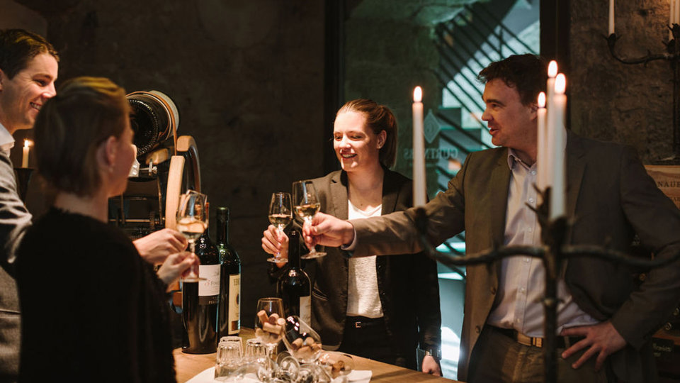 Vier Personen stossen im Weinkeller vom Gewölbekeller mit einem Glas Wein an.