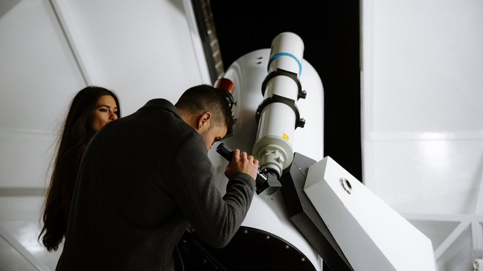 Ein Mann schaut durch das Teleskop in der Gurten-Sternwarte und eine Frau schaut ihm dabei zu.