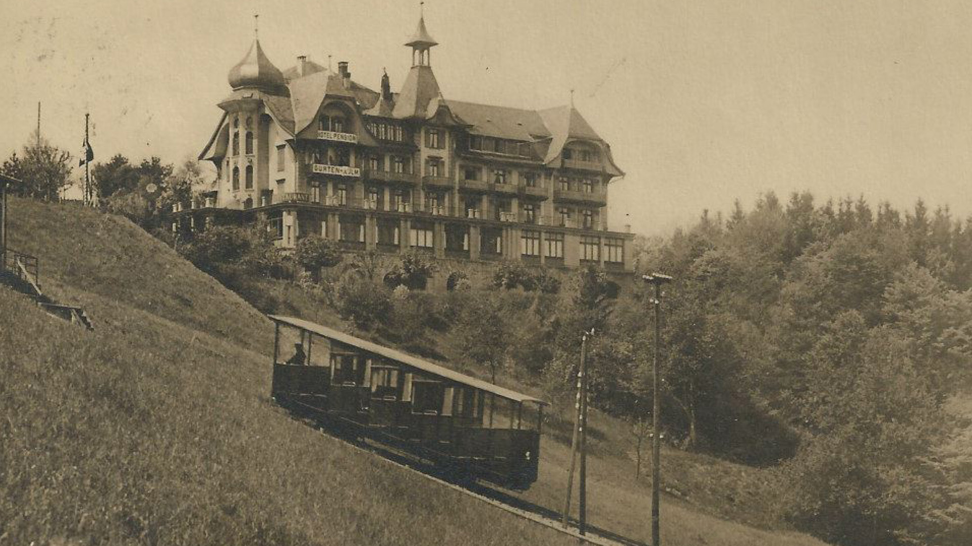 Eine Schwarzweissaufnahme eines Wagongs der Gurtenbahnvor dem Kulm-Bebäude.