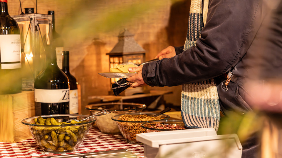 Gast stellt im Winterdorf auf dem Gurten einen Teller mit Raclette und Beilagen an einem Buffet zusammen.