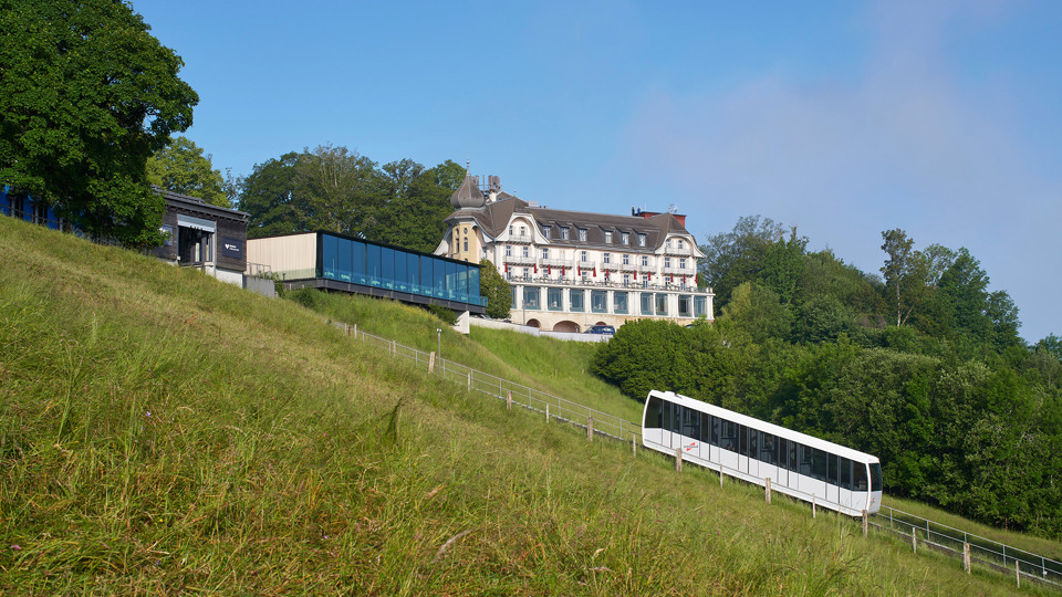 Die Gurtenbahn bei Tag vor dem Kulm-Gebäude und der Eventlocation Pavillon.
