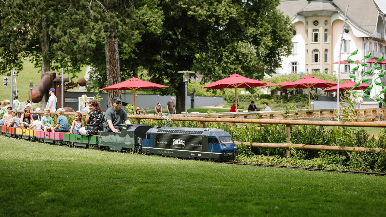 Kleineisenbahn fährt an Zaun vorbei in Spielpark