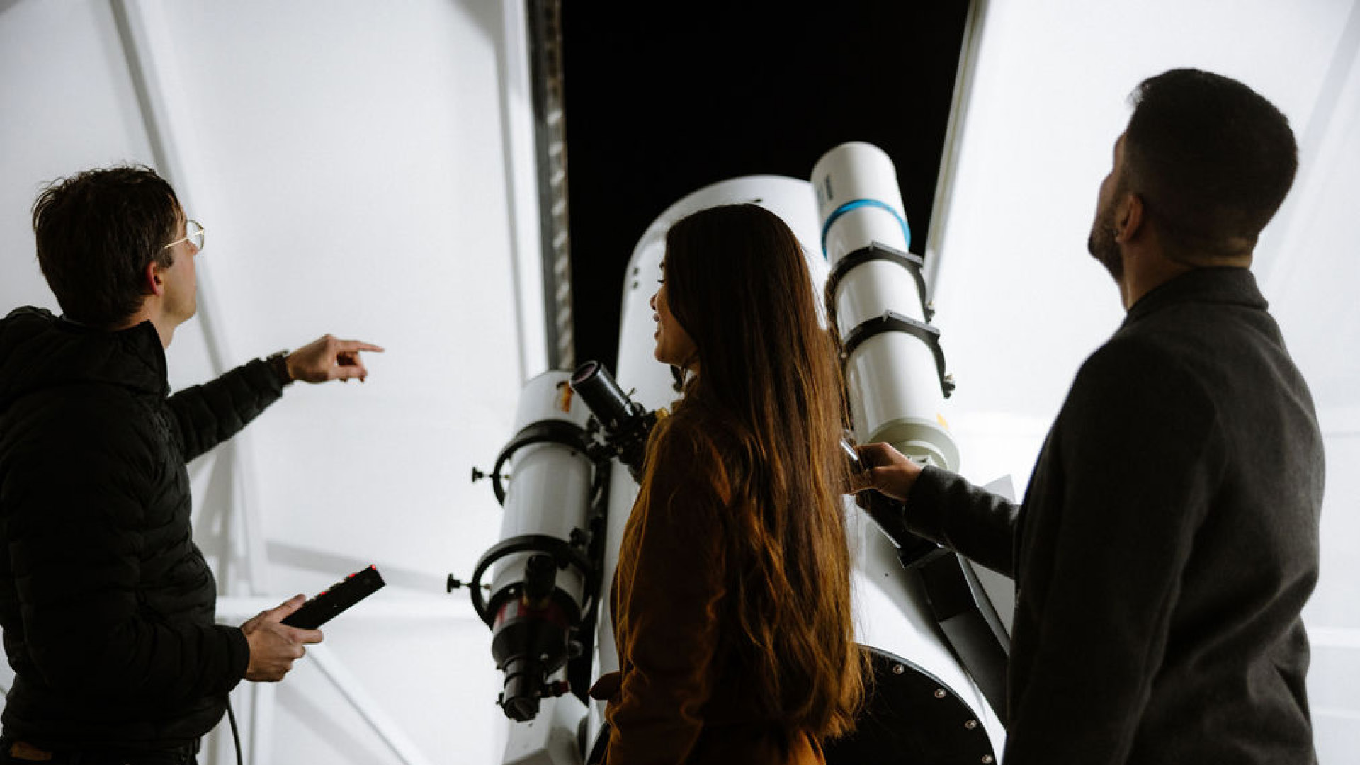 Drei Personen stehen in der Sternwarte und bekommen von einem Experten den Himmel erklärt.