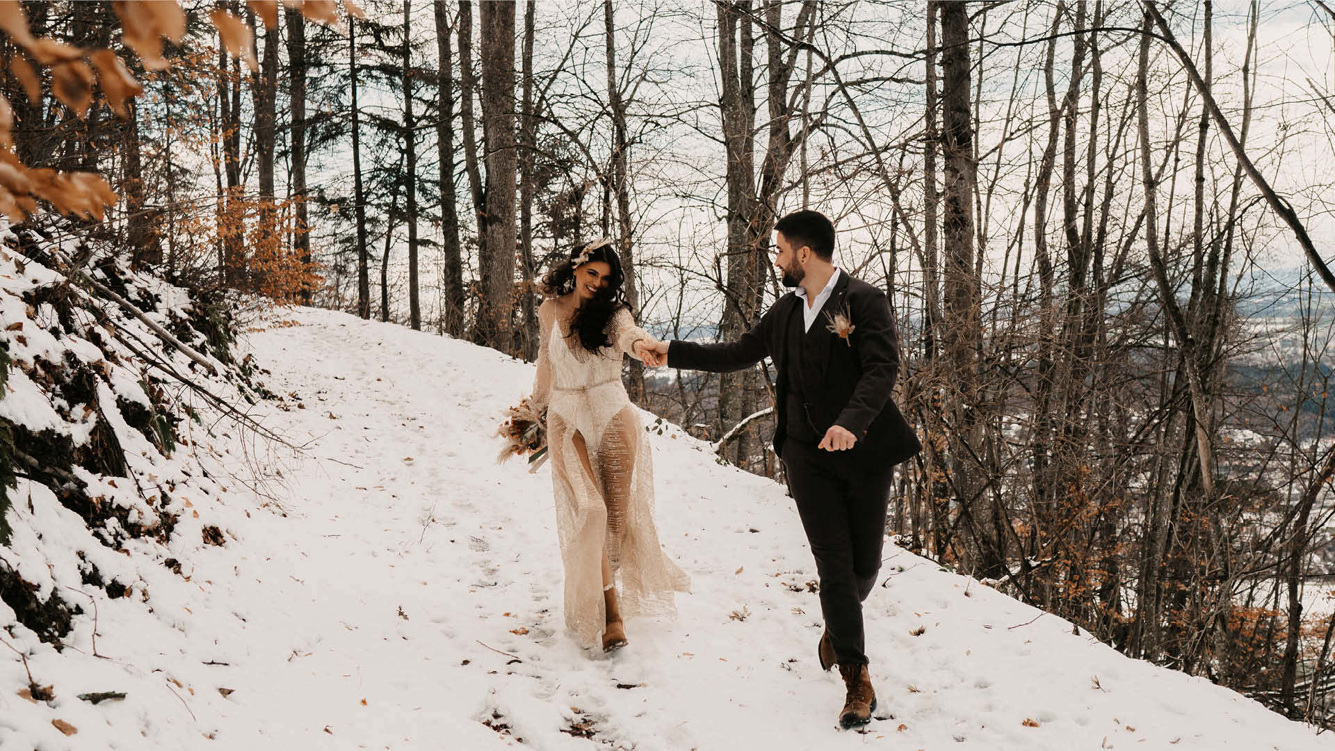 Ein Hochzeitspaar geht gemeinsam auf dem verschneiten Weg Richtung talabwärts.