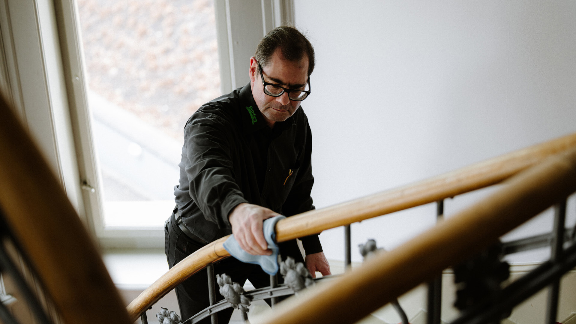 Eine Person in einem schwarzen Hemd, welch das Treppengeländer mit einem blauen Tuch putzt.
