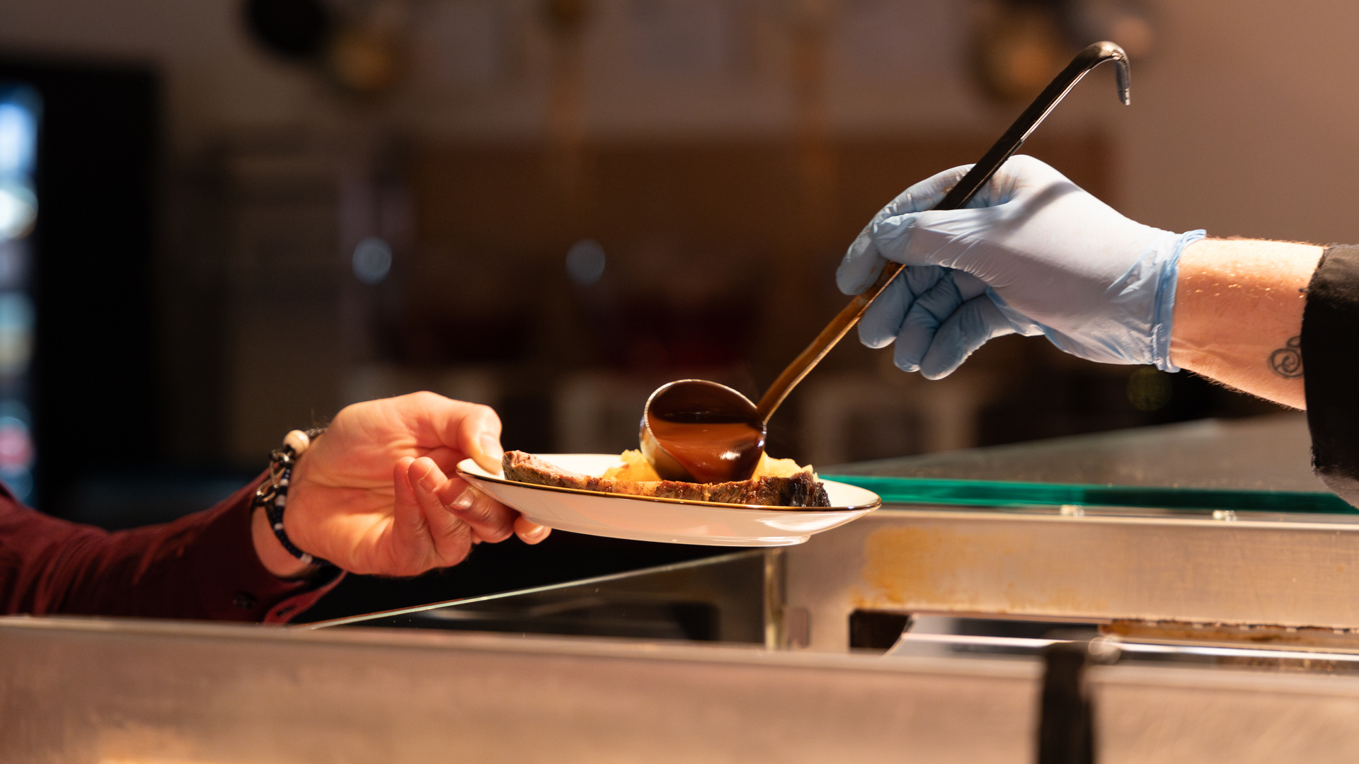 Ein Koch schöpft Sauce auf einen Teller, den ein Gast hinhält