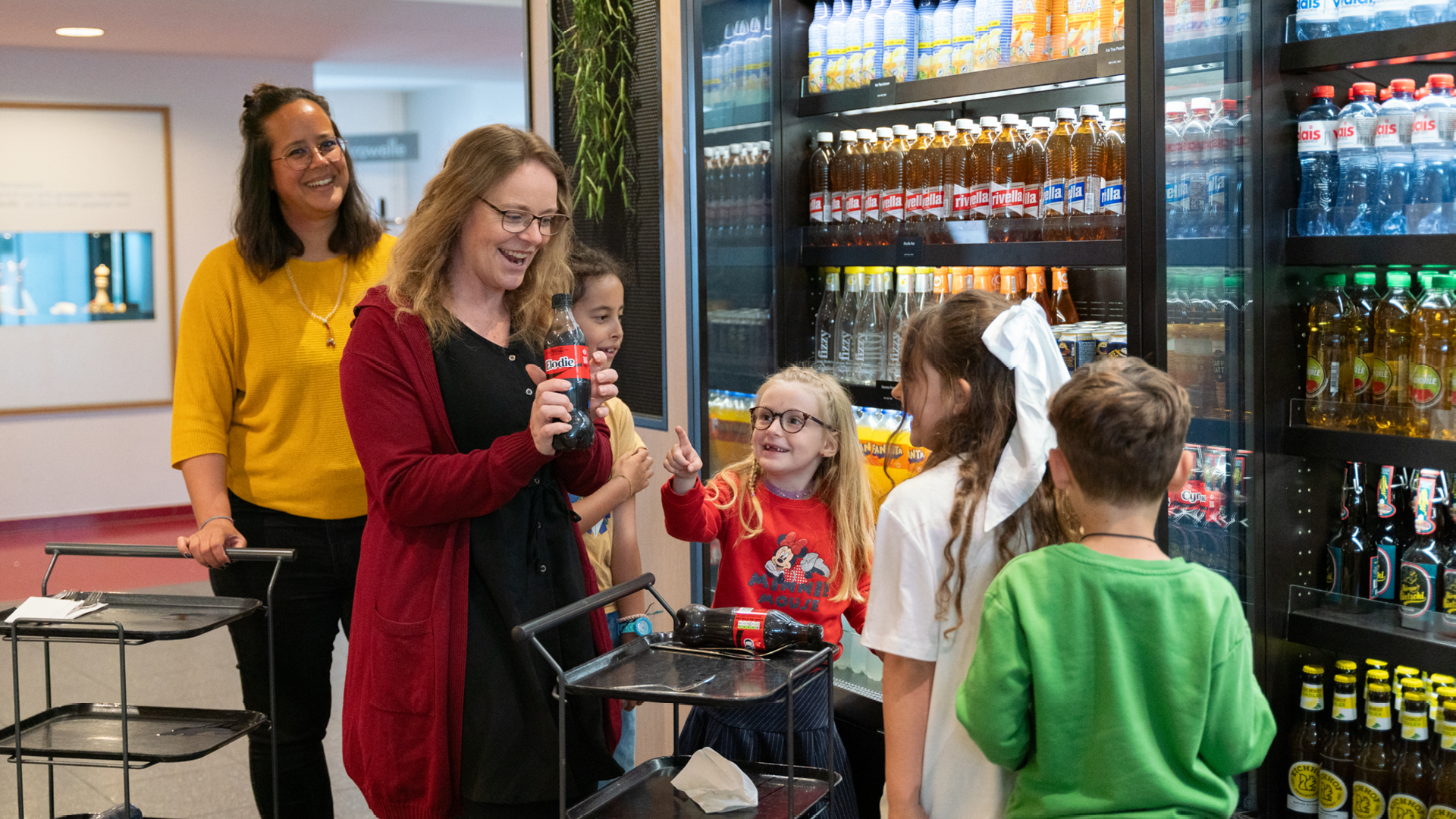 Fünf Personen welche sich Getränke aus dem Kühlregal nehmen. Die Person mit dem roten Jäckchen hält eine Flasche in der Hand.