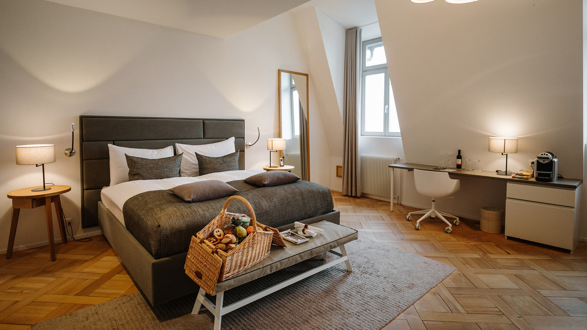 Ein Hotelzimmer mit einem grauen Bett, braunen Nachttischen, einem braunen Picknickkorb und einem Pult.
