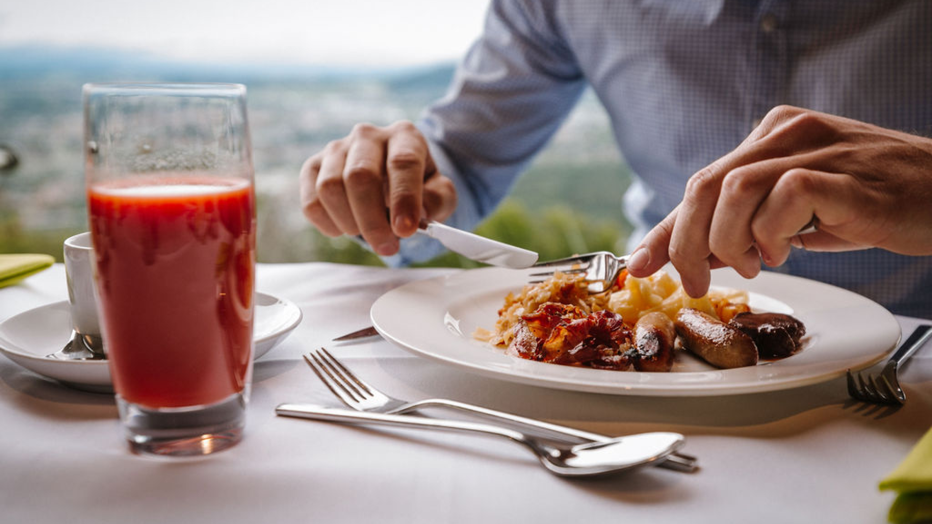 Mann am brunchen mit einem Teller mit Cipollata, Rösti und einem Glas Tomatensaft. Dahinter die Aussicht aus dem Pavillon. 