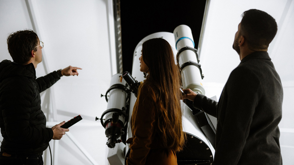 Drei Personen stehen in der Sternwarte und bekommen von einem Experten den Himmel erklärt.