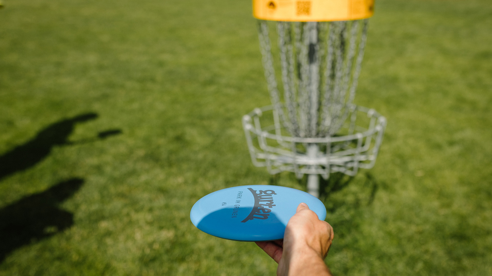 Person probiert blaus Frisbee in Discgolfkorbe zu treffen